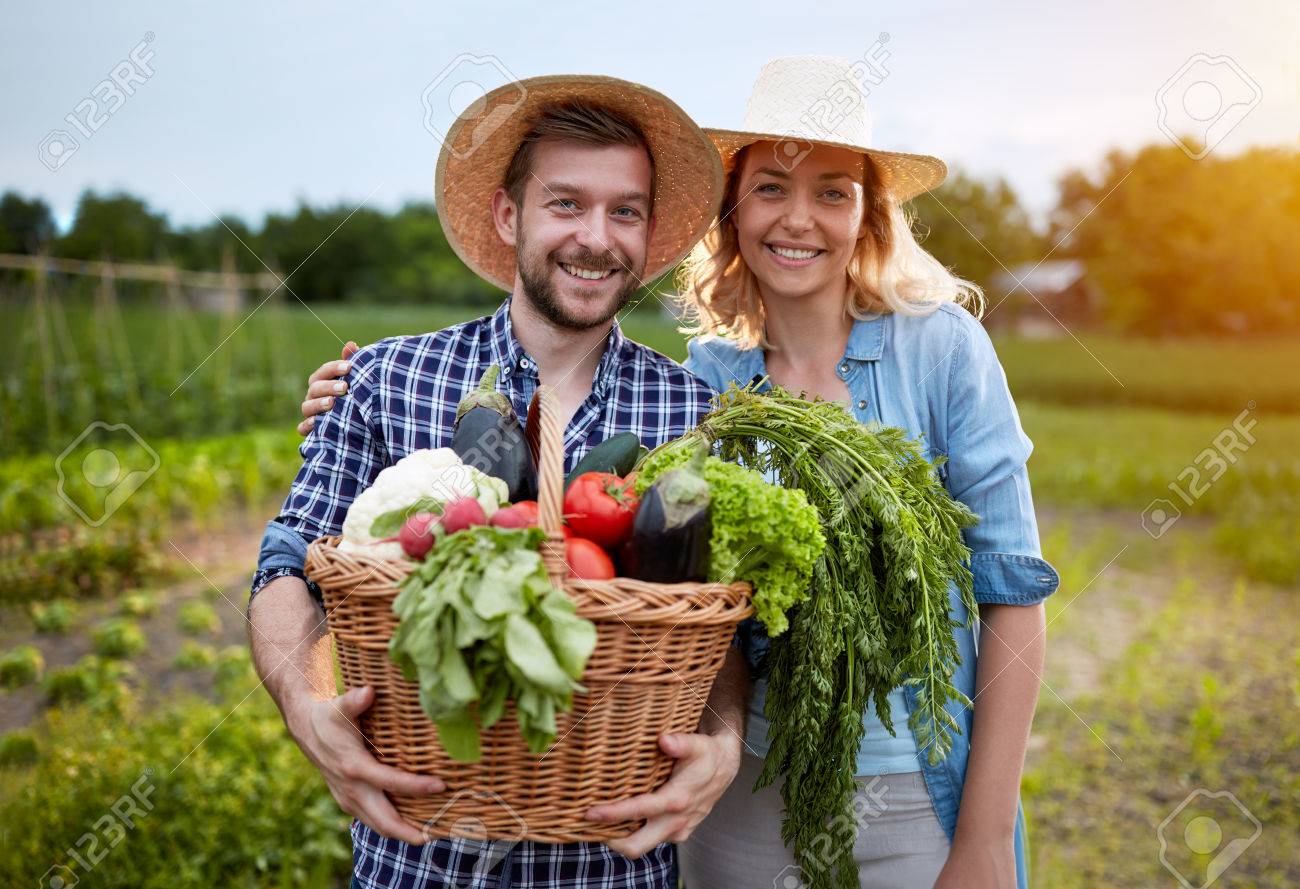 Nos producteurs, du coin jusqu’à votre assiette 2 Couple de maraîchers tenant un panier de légumes bio dans un champ.