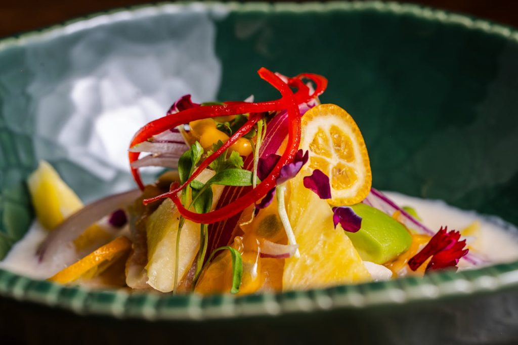 fresh-gourmet-ceviche-with-citrus-and-herbs-29188619 Vibrant ceviche dish with citrus, herbs, and colorful garnishes in a green bowl.